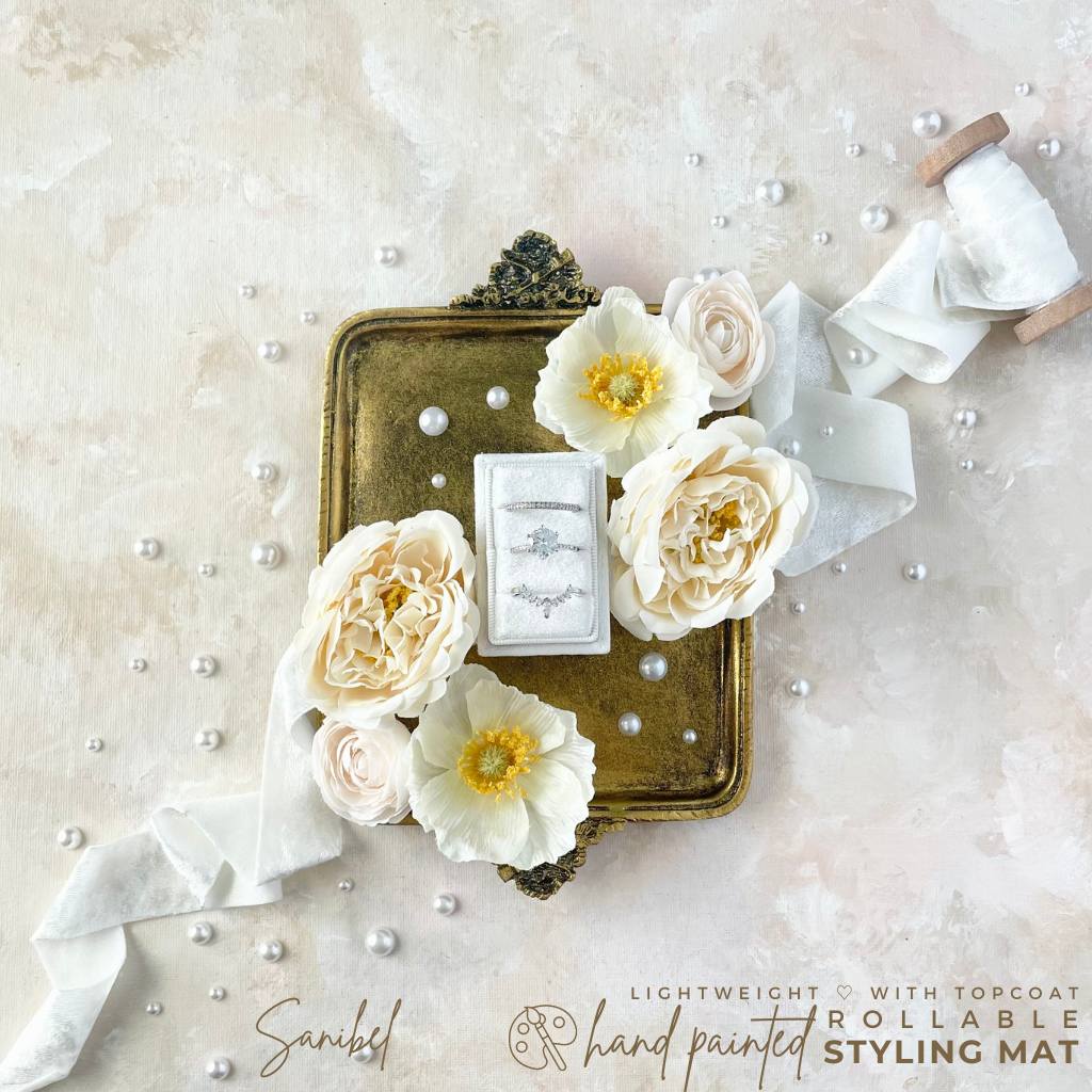Mini tray with white roses and a 3 slot velvet ring box styled with White Velvet Ribbon ½ unrolled off its wood spool on a diagonal line.  There are small styling pearls placed randomly around the tan color backdrop