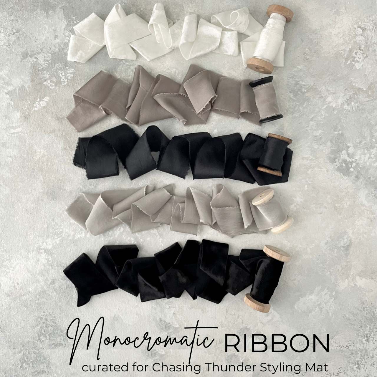 Ribbon Flat Lay kit in a monochromatic color pallet.  Ribbon is unrolled, White velvet ribbon, light cool gray silk ribbon, warm gray ribbon, black silk ribbon, and black velvet ribbon.  All ribbon is wrapped on wooden spools.  Styled on hand painted light gray styling mat