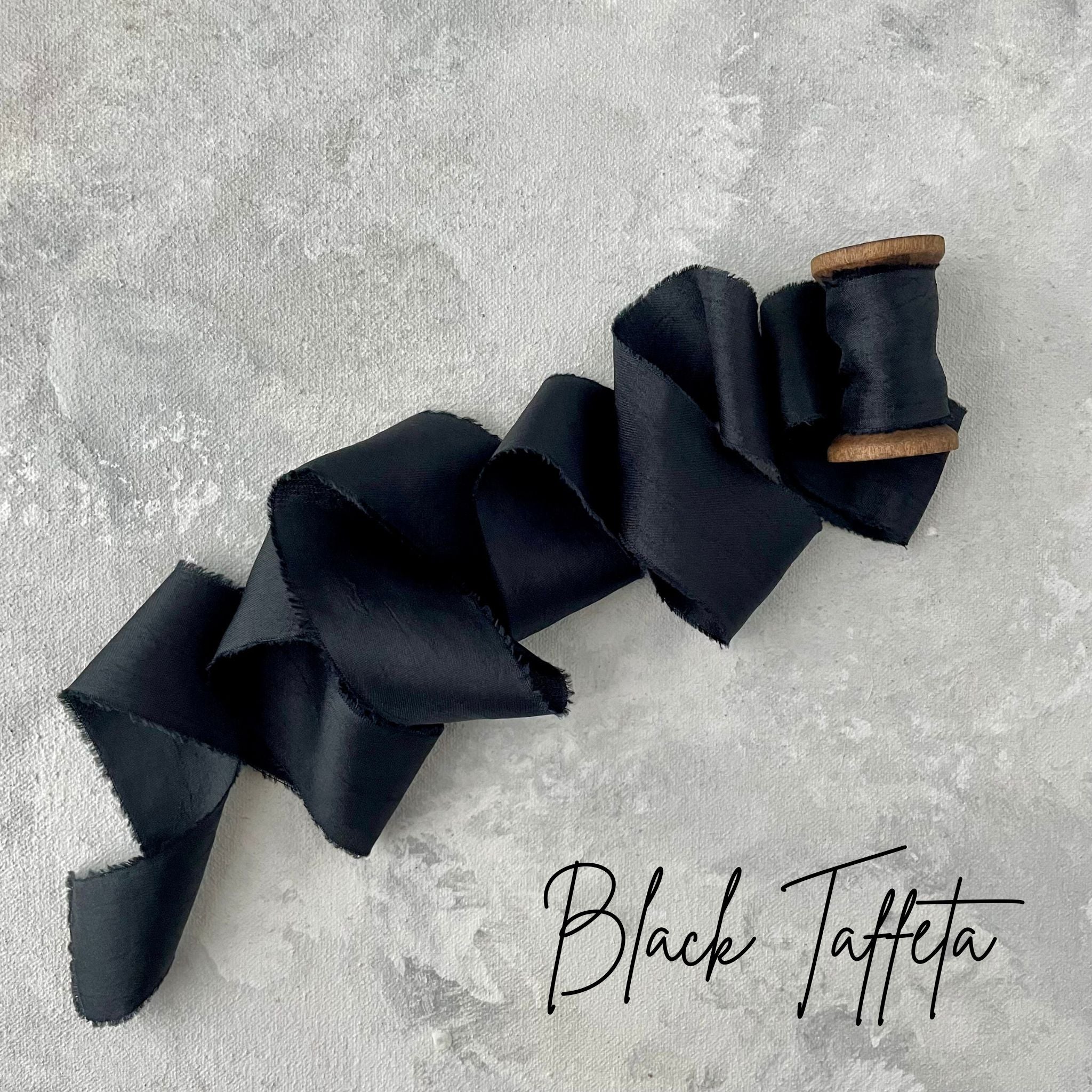 Black Silk ribbon on a spool unrolled on a diagonal styled on a light gray hand painted styling mat