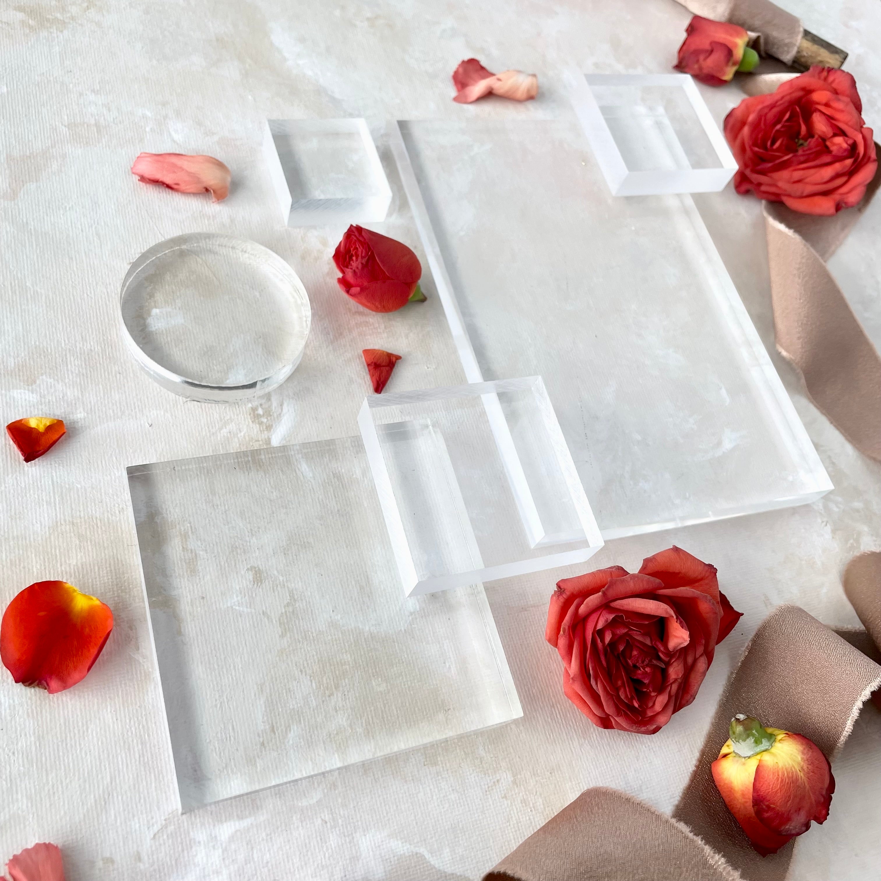 side angle shot of Clear Acrylic Styling Block Set including 4 different sized squares, one large rectangle, and one circle - styled with tan ribbon and roses - Flat Lays from Champagne & GRIT