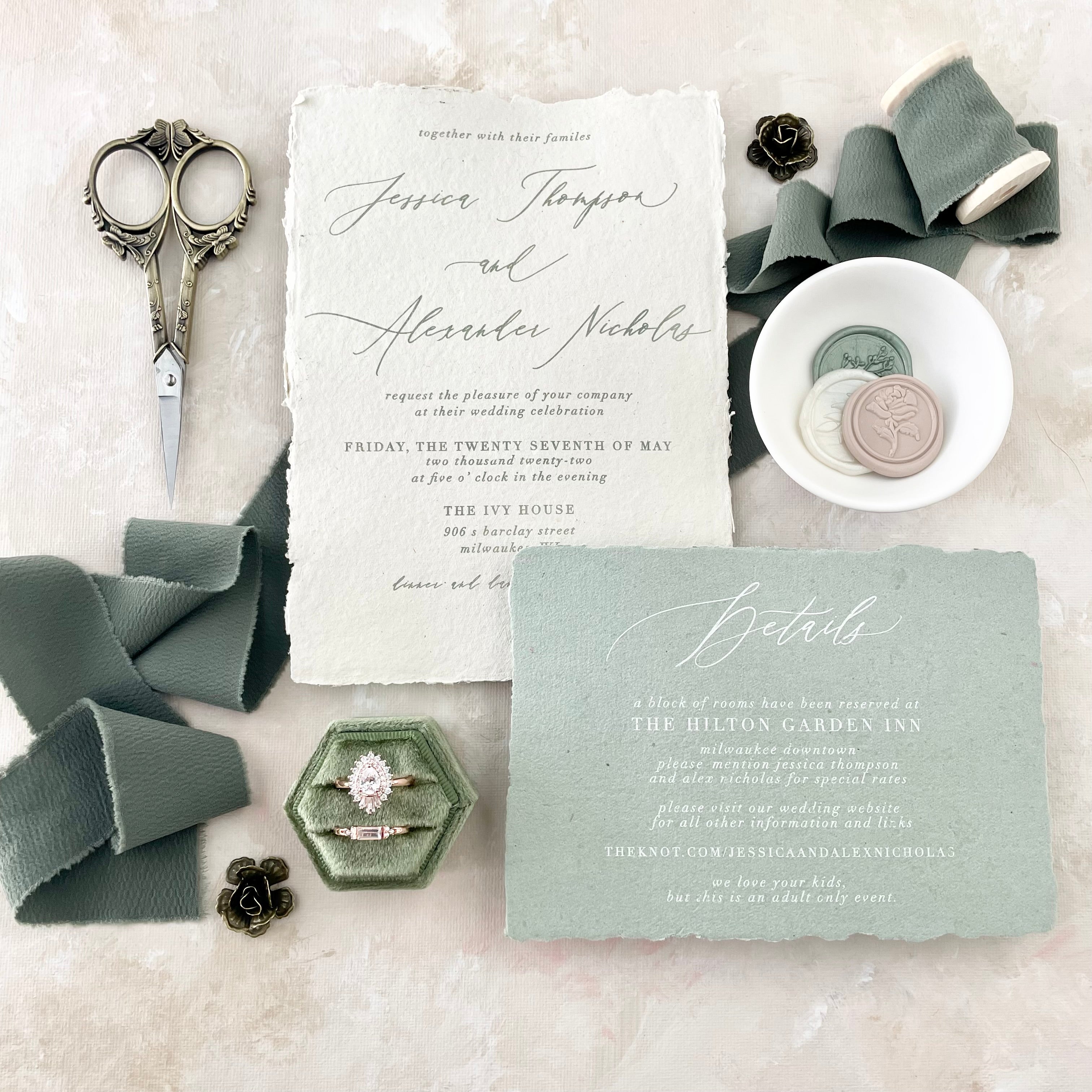Sage green flat lay including sage green ring box, sage green ribbon, wedding invitation, vintage scissors, 3 wax seals in white dish and two metal styling flowers  - Flat lay props from Champagne & GRIT