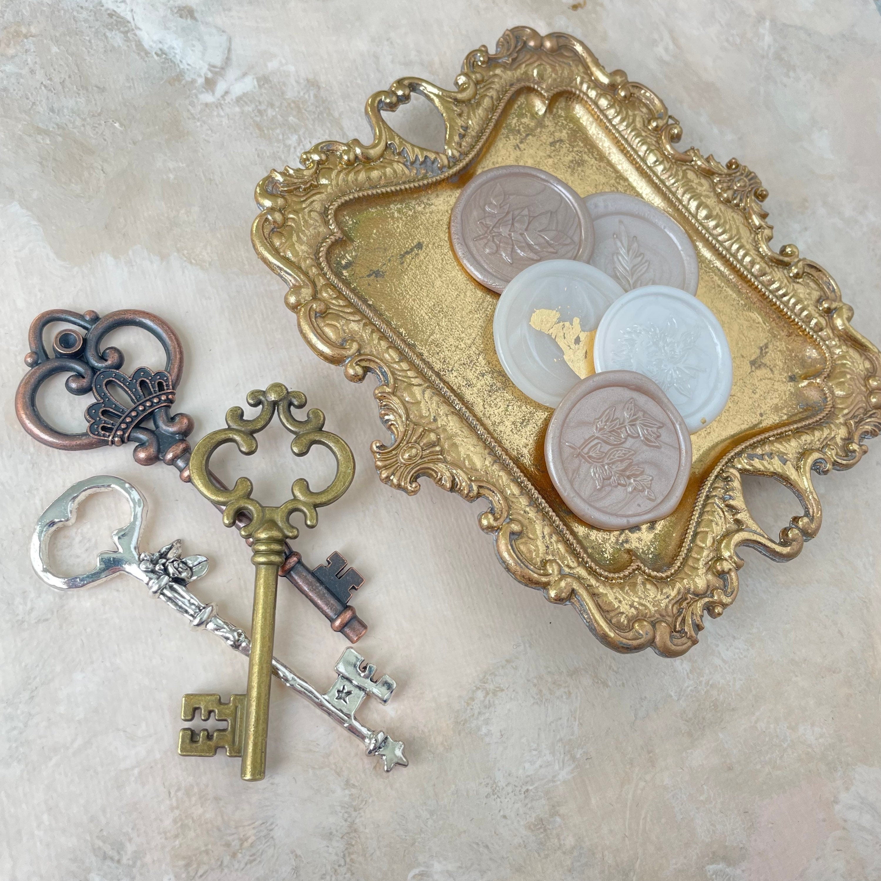5 champagne and ivory wax seals on gold tray beside one gold key, one bronze key, and one silver key these are must have flat lay props from Champagne & GRIT