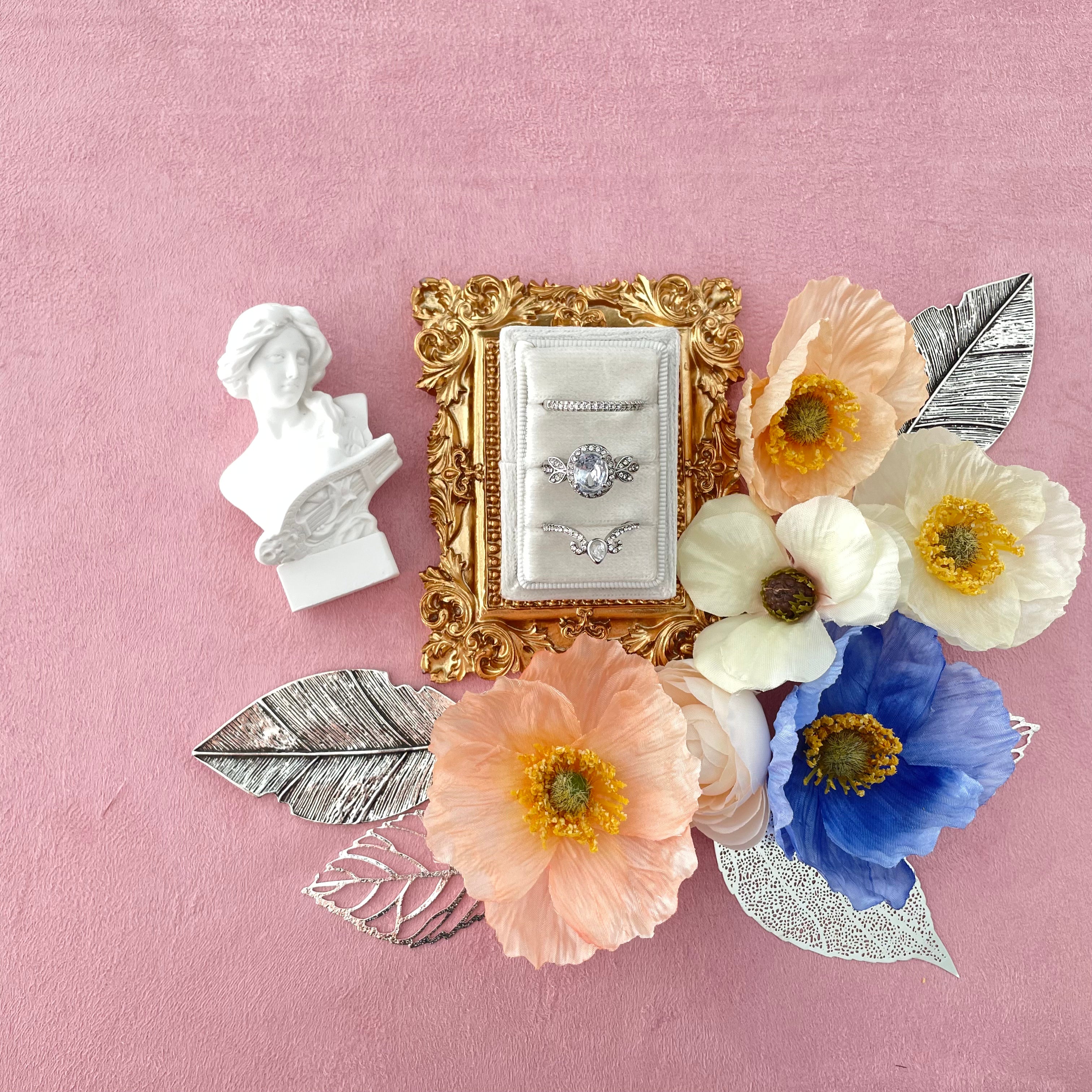 Small vintage figurine and 3 slot ring box on gold tray with 4 styling leaves and pink, white and blue florals - wedding flat lay props from Champagne & GRIT