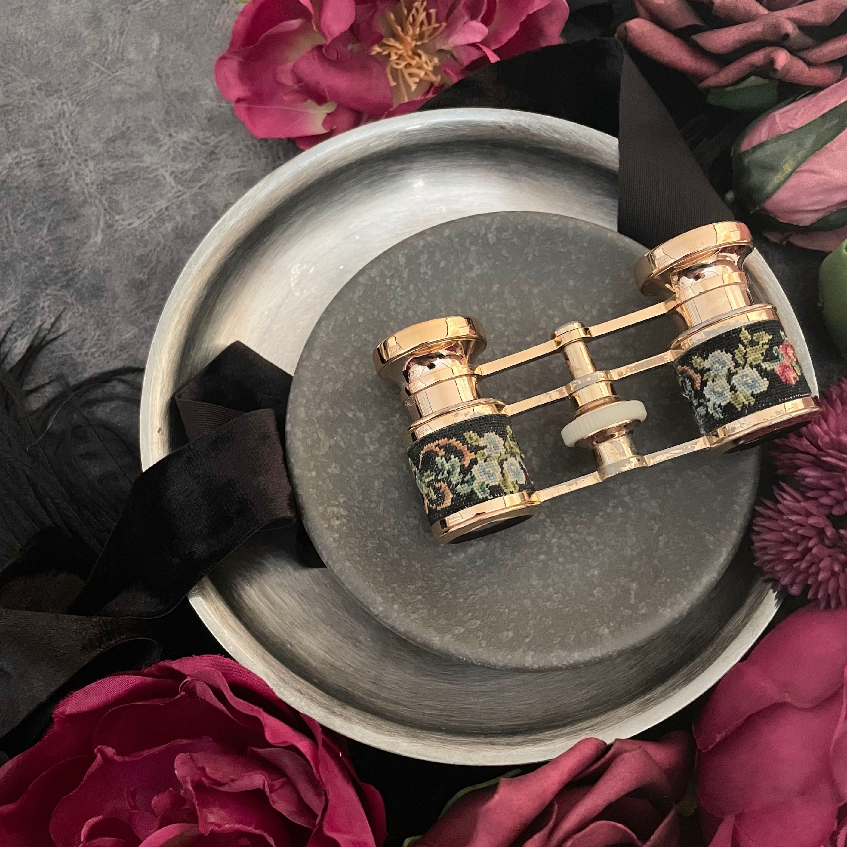 Needle point black opera glasses with pastel flowers styled on a mini black concrete dish layered on top of a black velvet ribbon and vintage silver round tray with hot pink peonies.