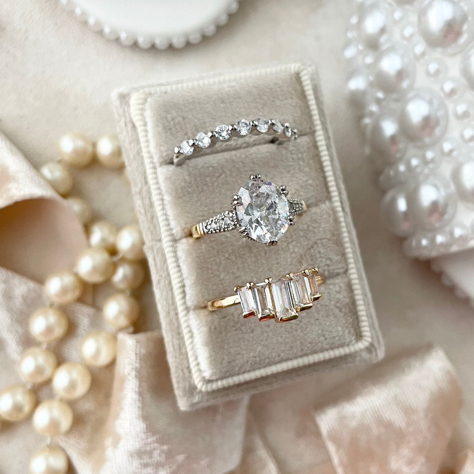 Three diamond rings in a 3 slot Champagne Velvet Ring Box.  Styled with a Velvet ribbon & stand of pearls  