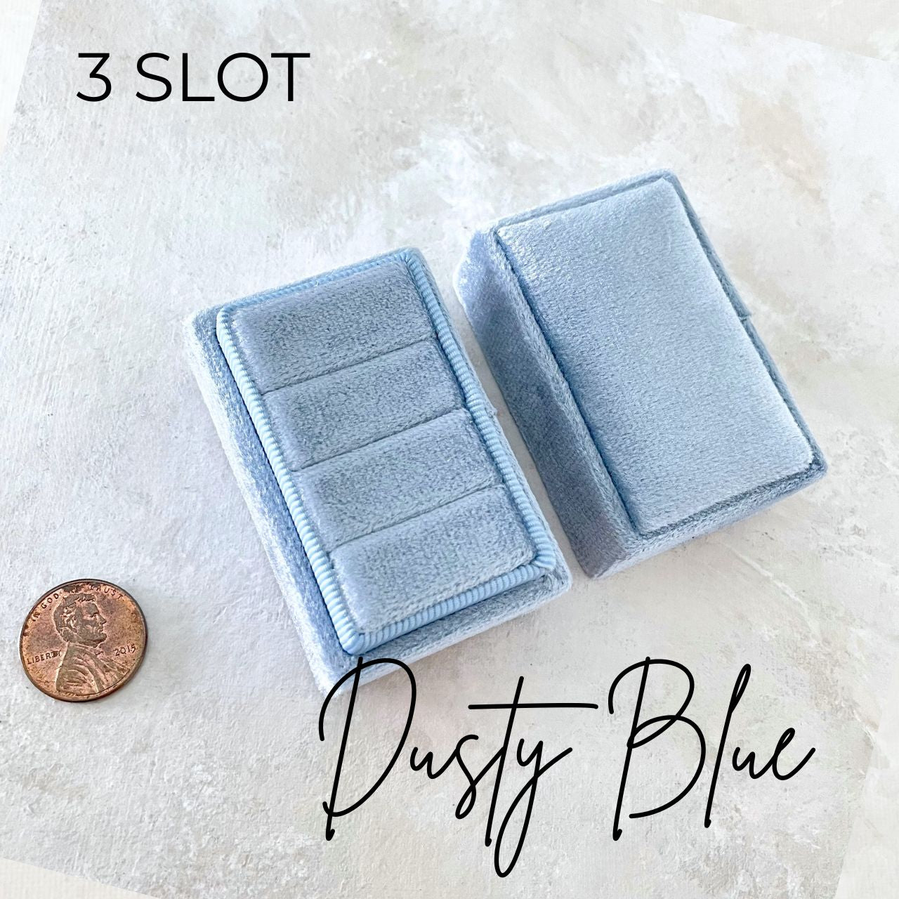 dusty blue velvet ring box, rectangle shape.  there is a penny in the photo scale.  