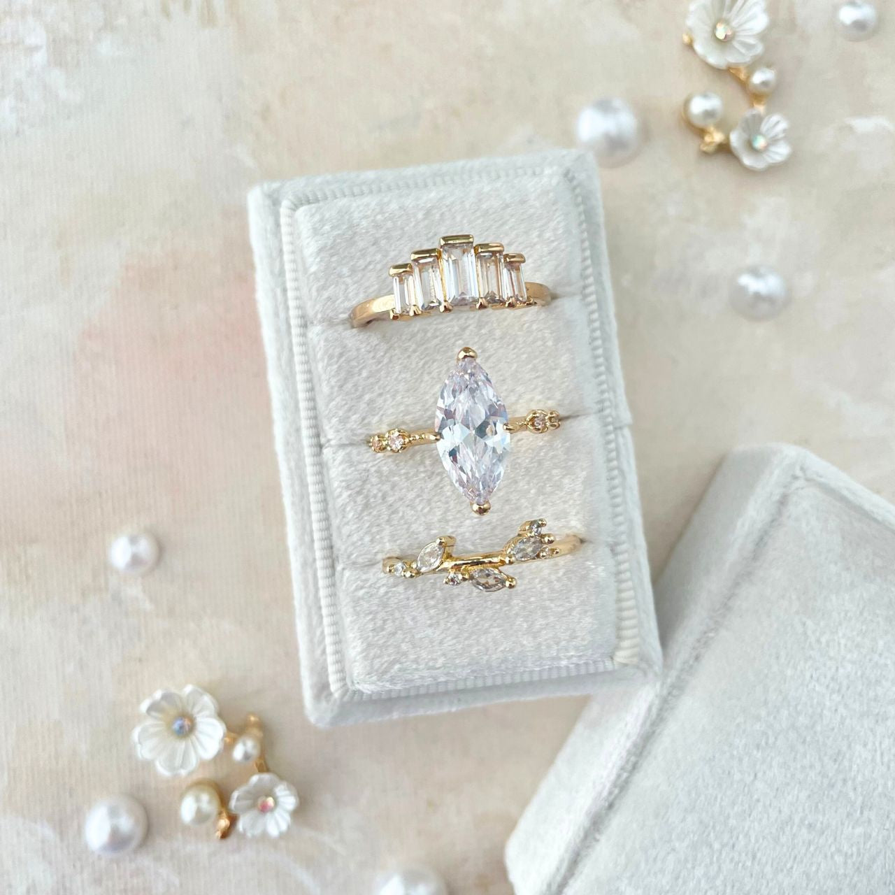 White Velvet rectangle ring box with 3 gold rings.  Styled with scattered pearls and flowers.