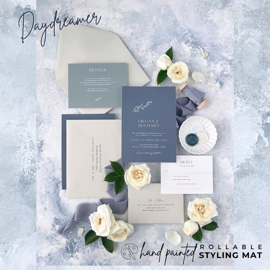 Invitation Suite Flat Lay Styled on Dusty Blue Background.  Rollable Dusty Blue Styling Mat Showcases silk blue flatlay ribbon, white roses & wedding invitation