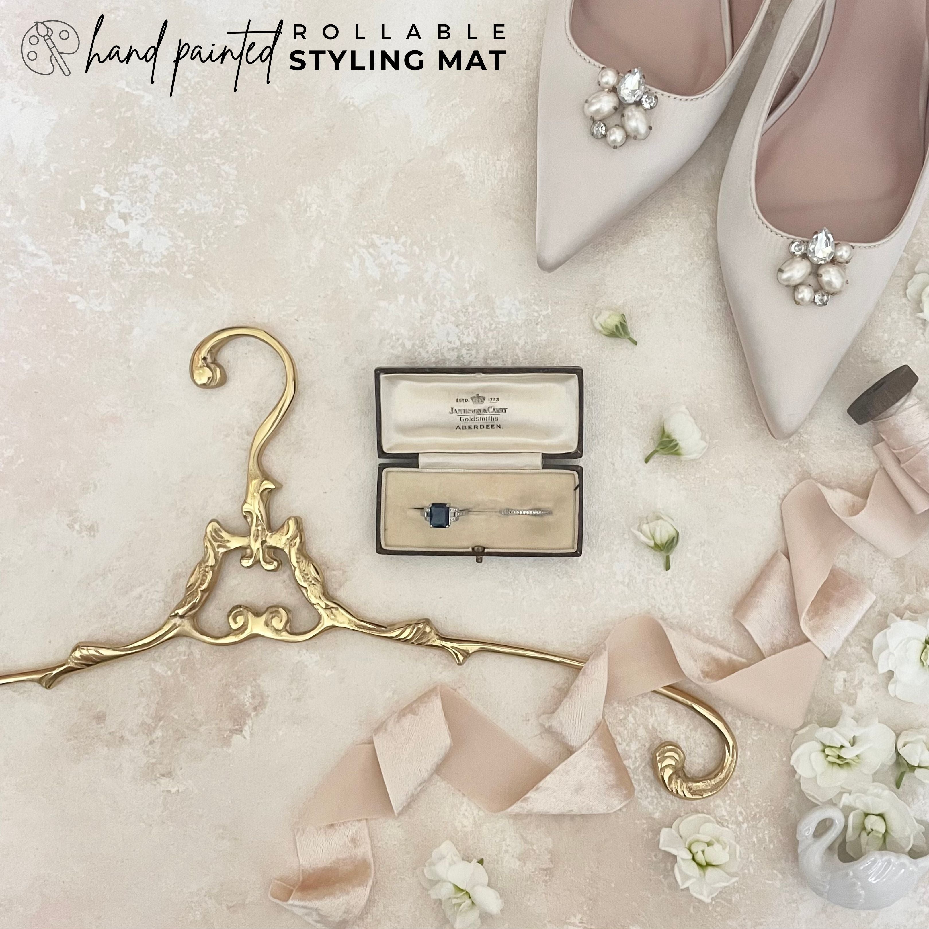 Hand Painted Neutral Flatlay Back Background.  Wedding day Flat lay detail styled on flat lay mat, featuring gold vintage hanger, vintage shoes, champagne velvet ribbon.  Bridal detail is showcasing Rollable Styling mat.