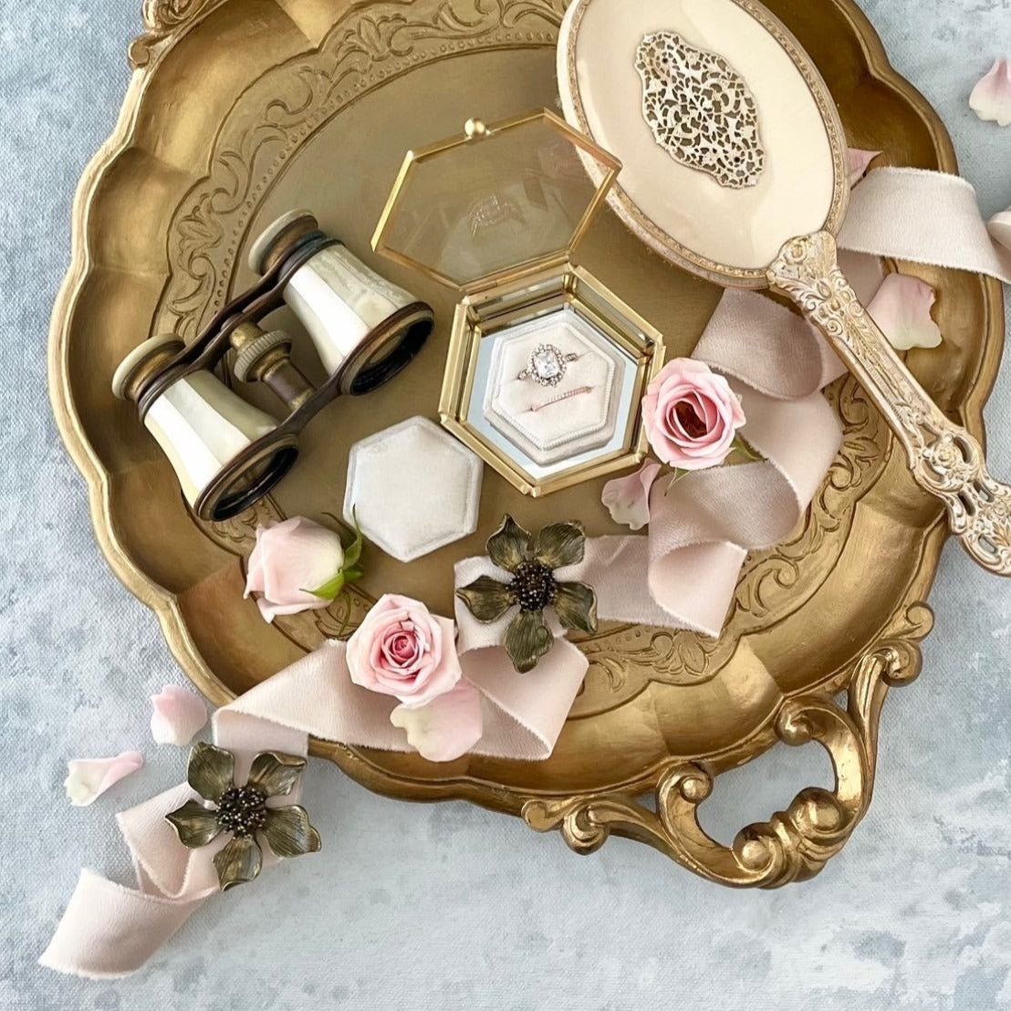 Large gold flat lay tray with vintage opera glasses, velvet ring box, gold vintage brush, dusty pink ribbon, light pink roses, and two  metal styling flowers  - Flat lay props from Champagne & GRIT