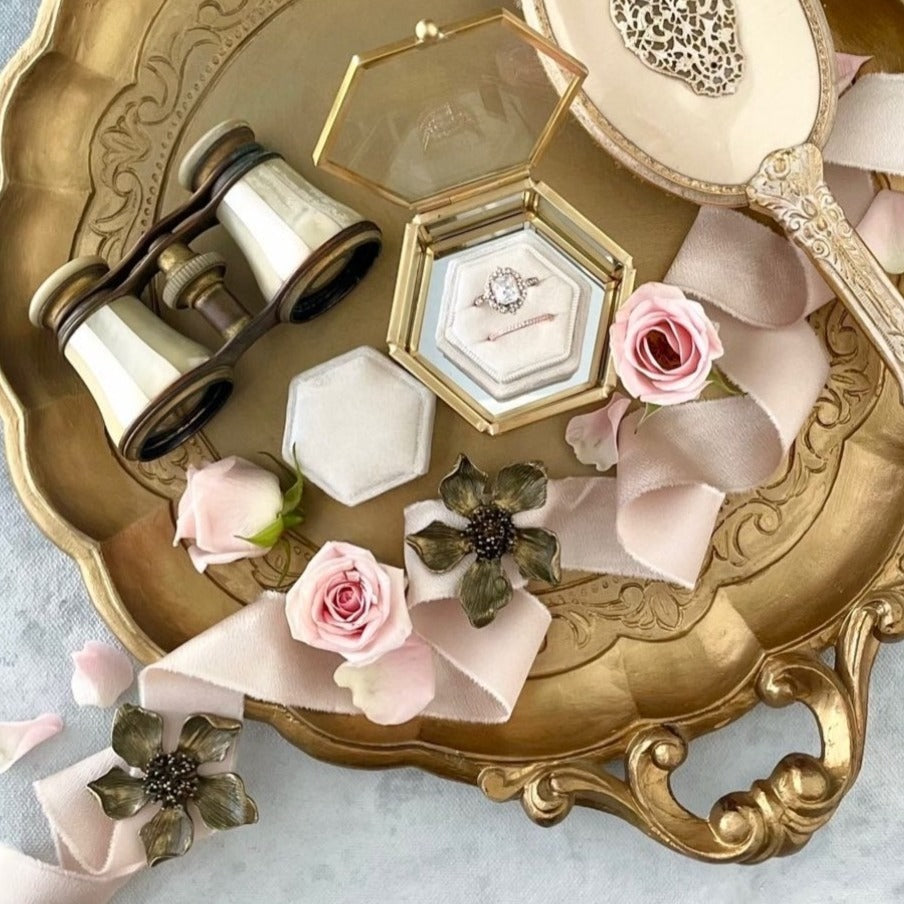 Large gold flat lay tray with vintage opera glasses, velvet ring box, gold vintage mirror, dusty pink ribbon, light pink roses, and two  metal styling flowers  - Flat lay props from Champagne & GRIT