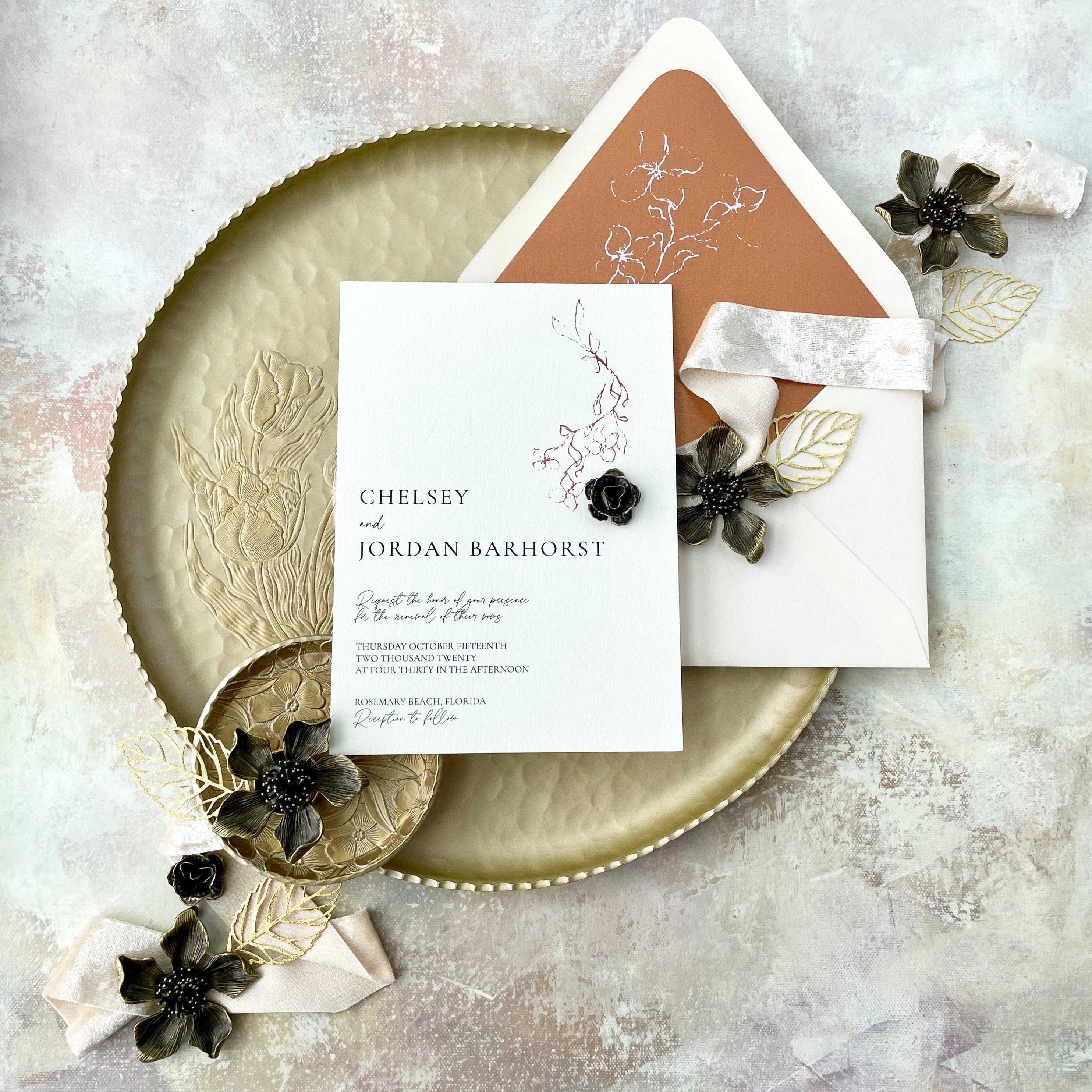 Floral wedding invitation styled with champagne velvet ribbon, two gold dishes, gold leaves, 3 large metal styling flowers, and 2 mini bronze styling flowers -  Flat lay props from Champagne & GRIT 