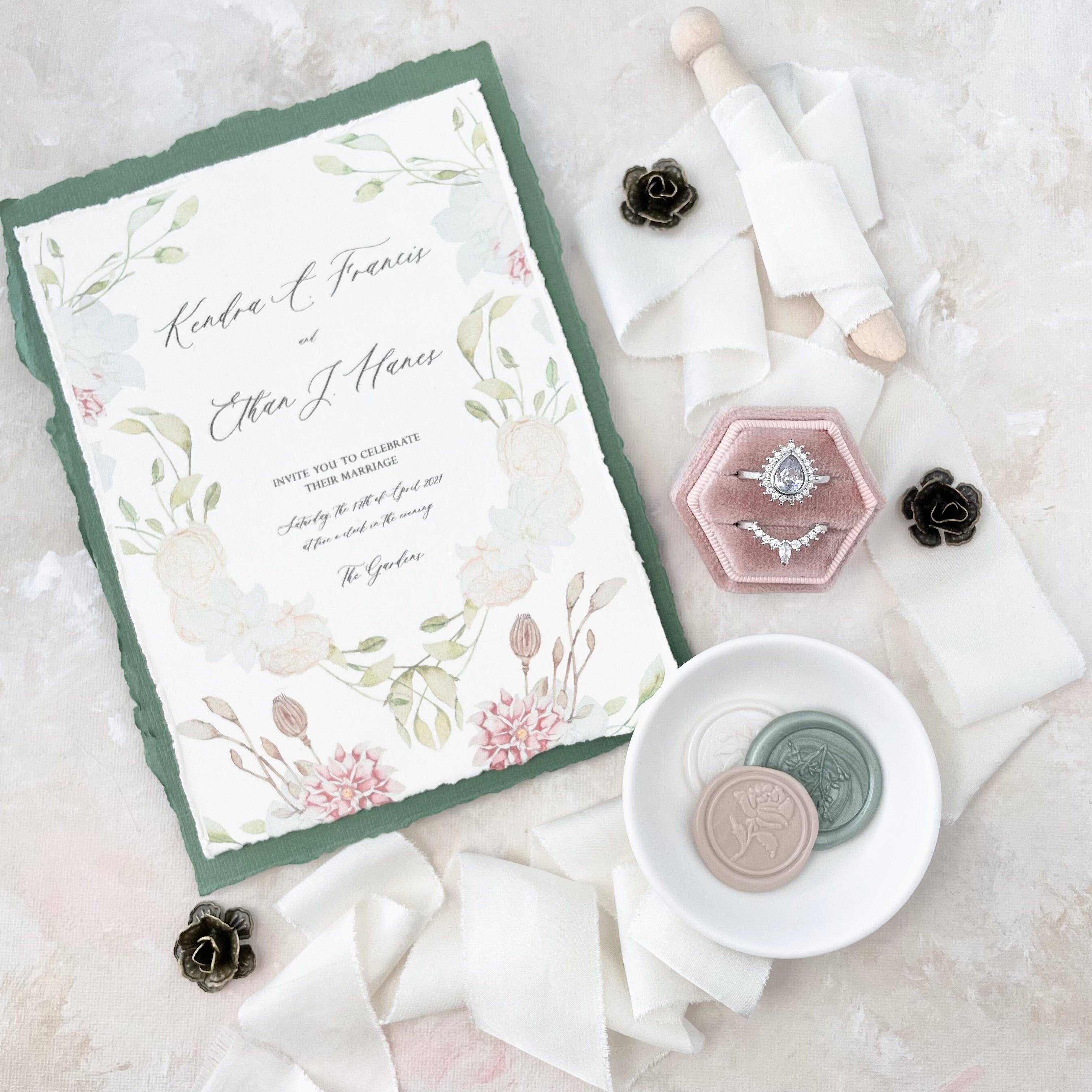 Floral wedding invitation with sage green envelope styled with dusty pink ring box, ivory ribbon, 3 wax seals in white dish and 3 metal styling flowers - flat lay props from Champagne & GRIT