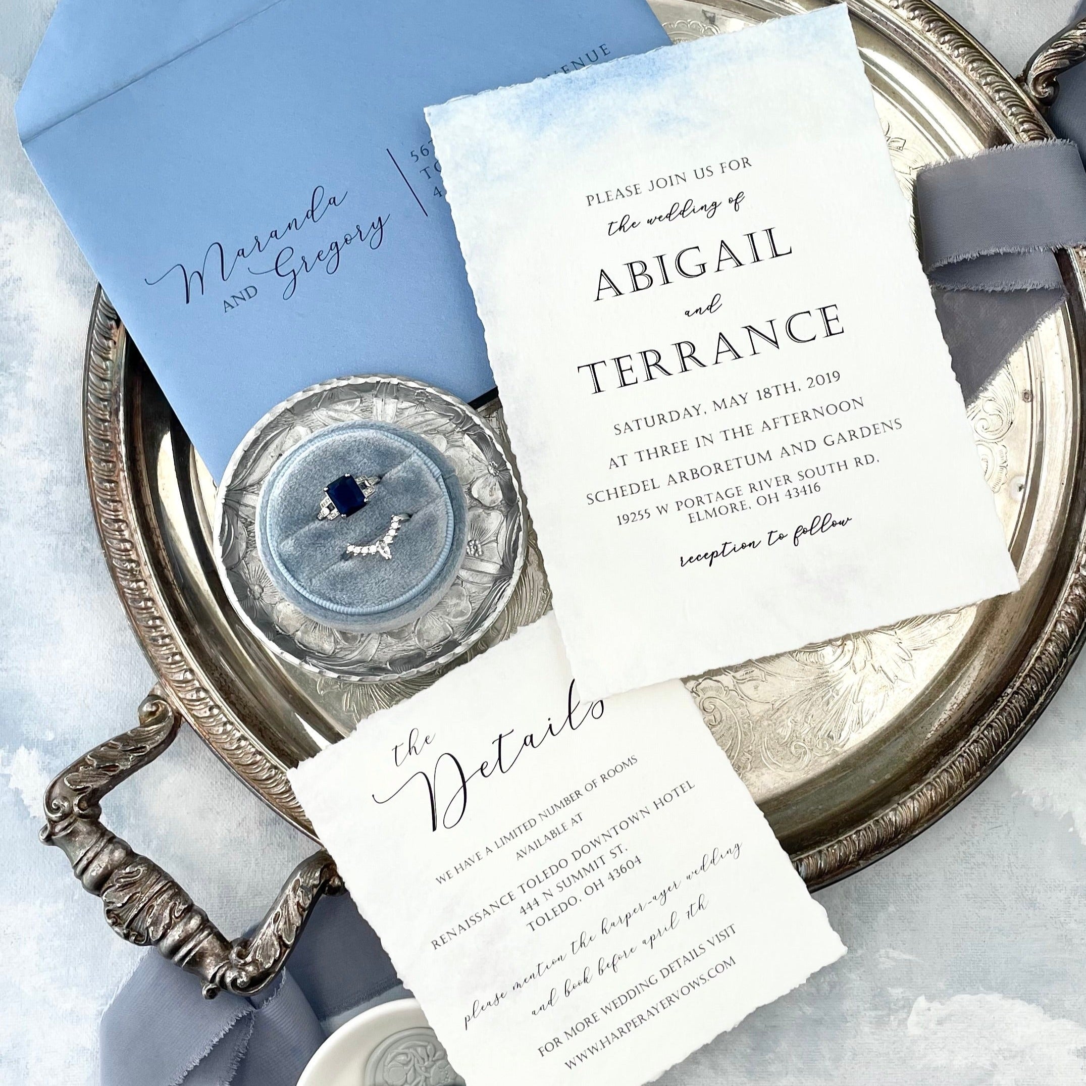 Dusty Blue Ring Box on silver tray, styled with dusty blue flat lay styling kit, white wedding invitation with blue envelope and dusty blue ribbon - wedding flat lay props from Champagne & GRIT