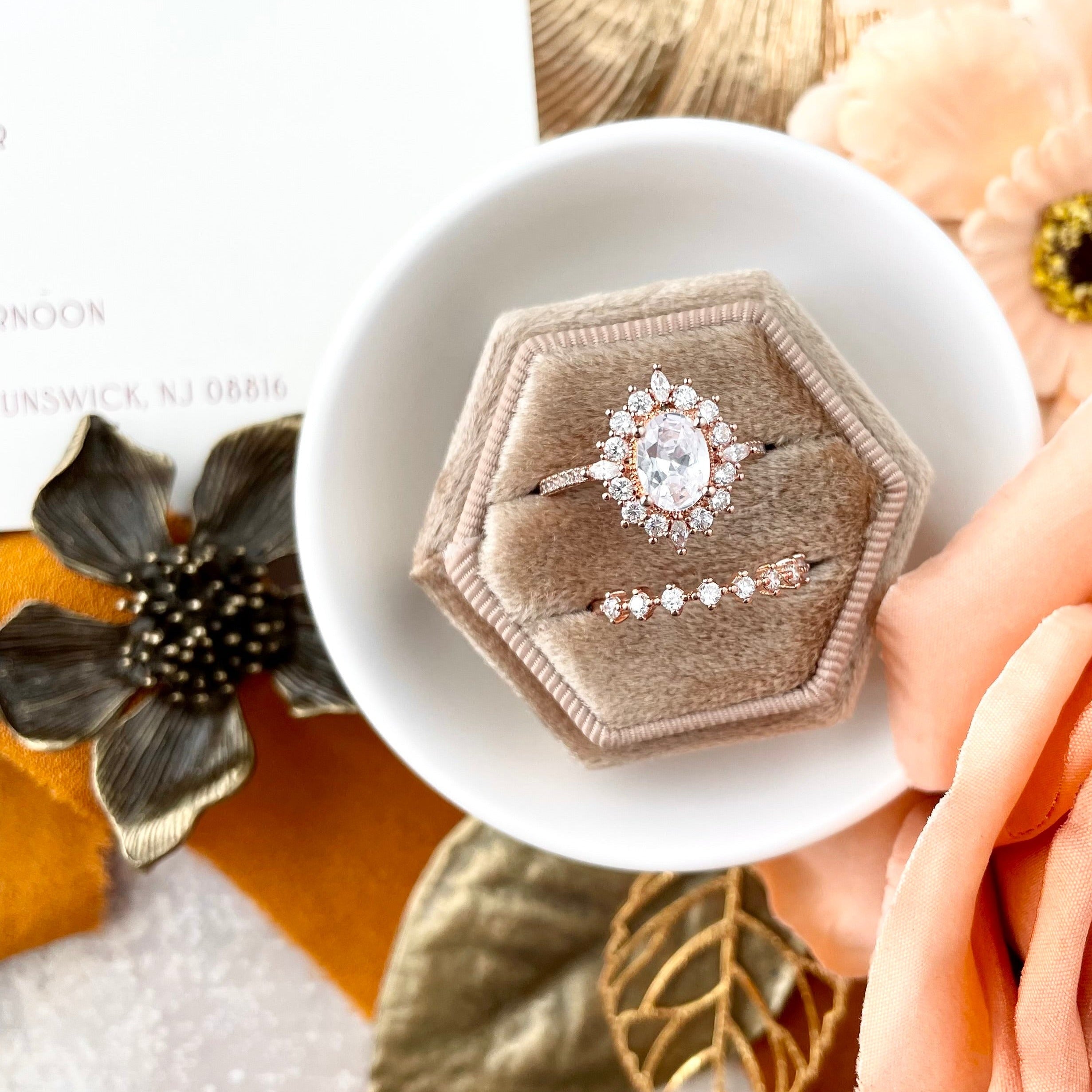 Close up of Champagne velvet ring box in white dish styled with blush artificial flowers and one metal styling flower - Flat lay props from Champagne & GRIT