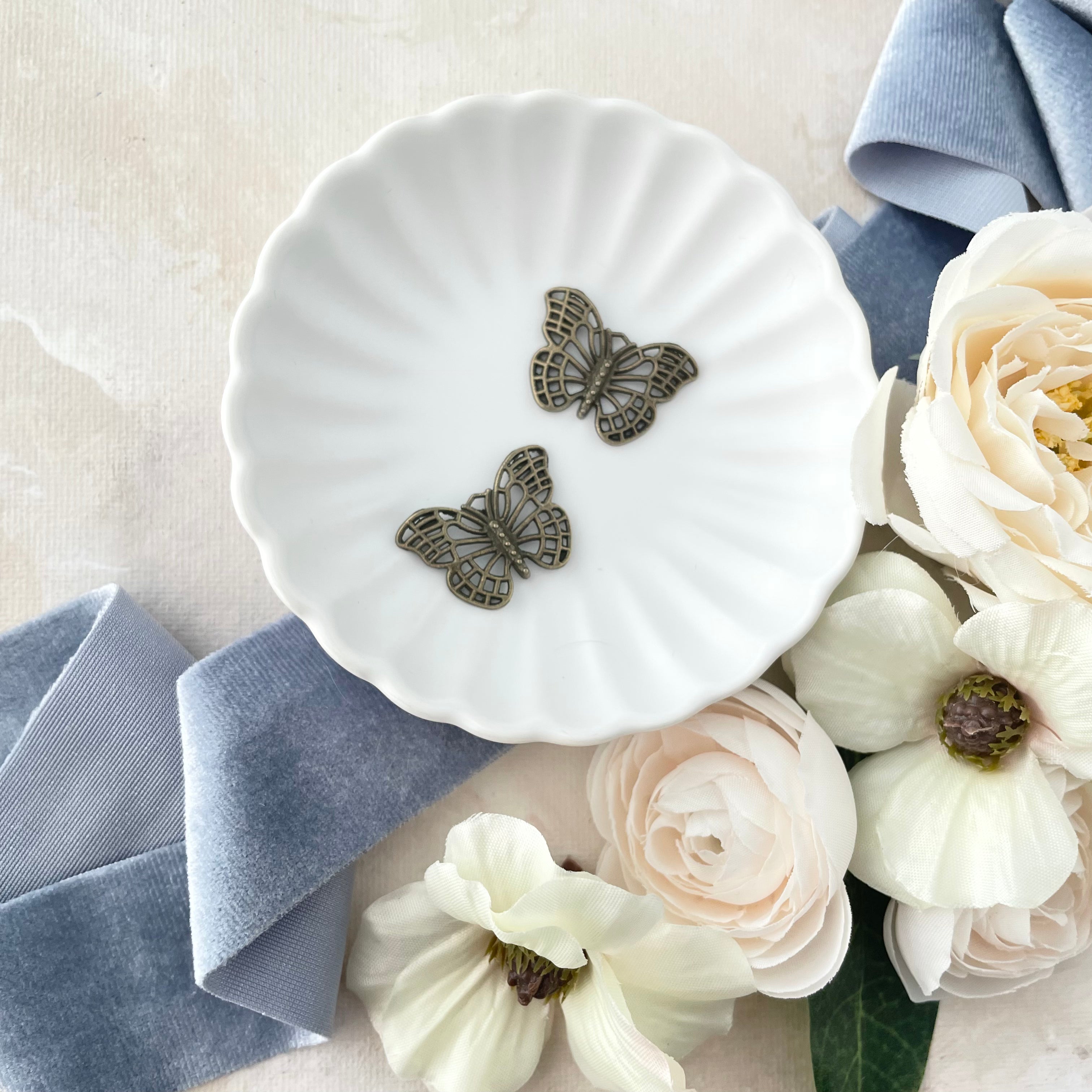 Close up of two bronze butterflies in white scalloped dish - wedding flat lay props from Champagne & GRIT