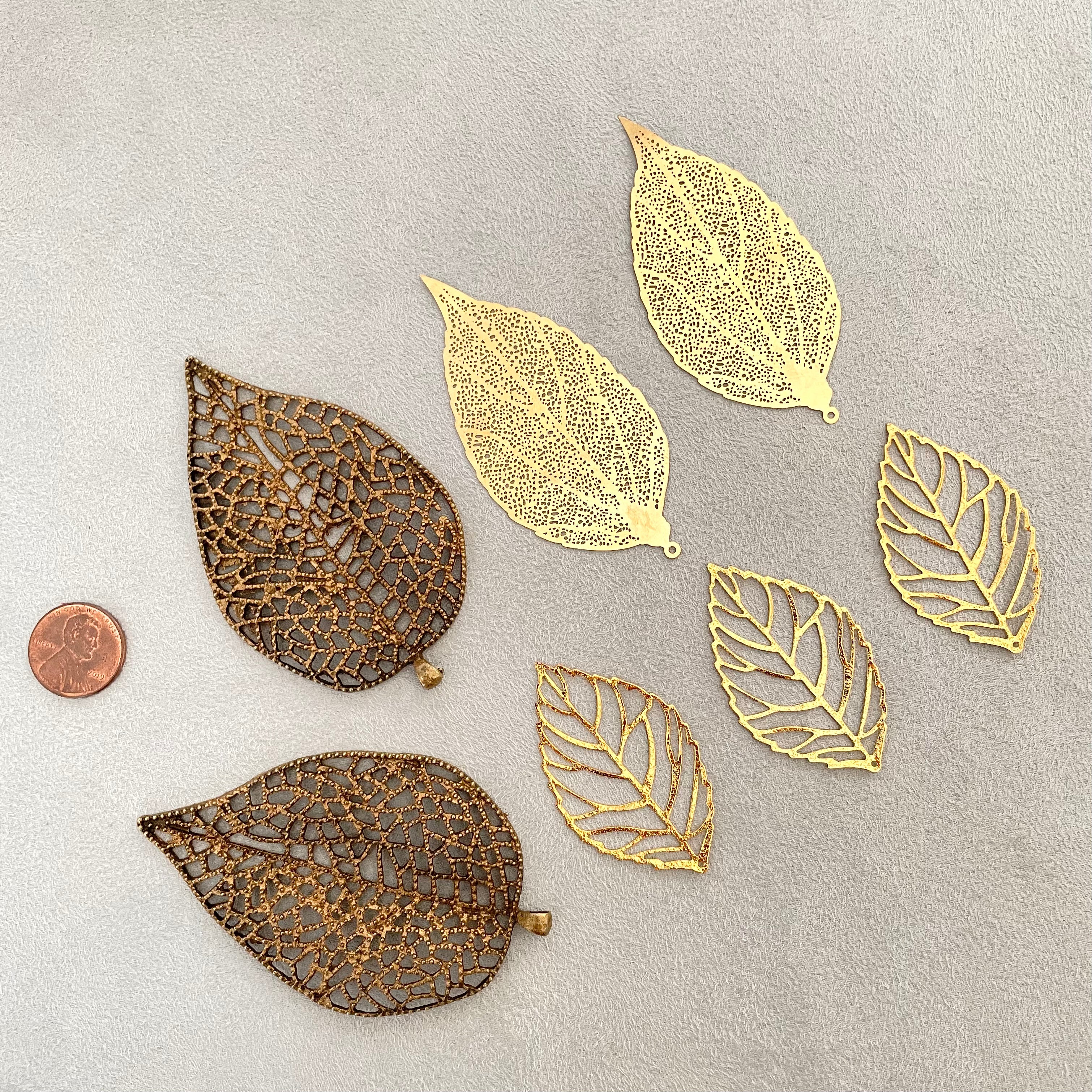 7 styling leaves including 3 gold leaves, 2 gold leaves that are larger and 2 large coco bronze leaves, penny beside for size reference  - flat lay props from Champagne & GRIT