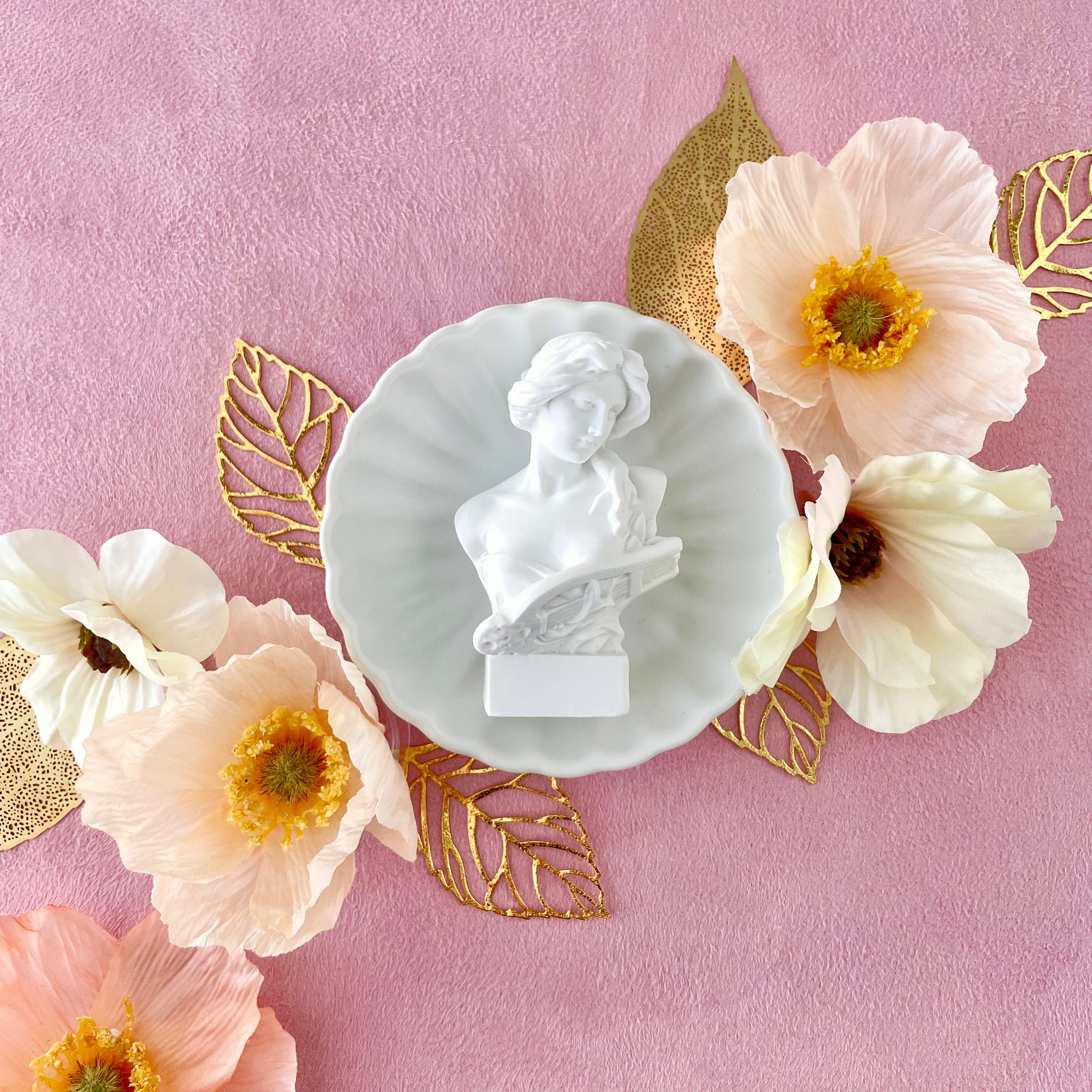 Small vintage figurine on white tray styled with 6 styling leaves including 3 gold leaves, 3 gold leaves that are larger with 5 florals - wedding flat lay props from Champagne & GRIT