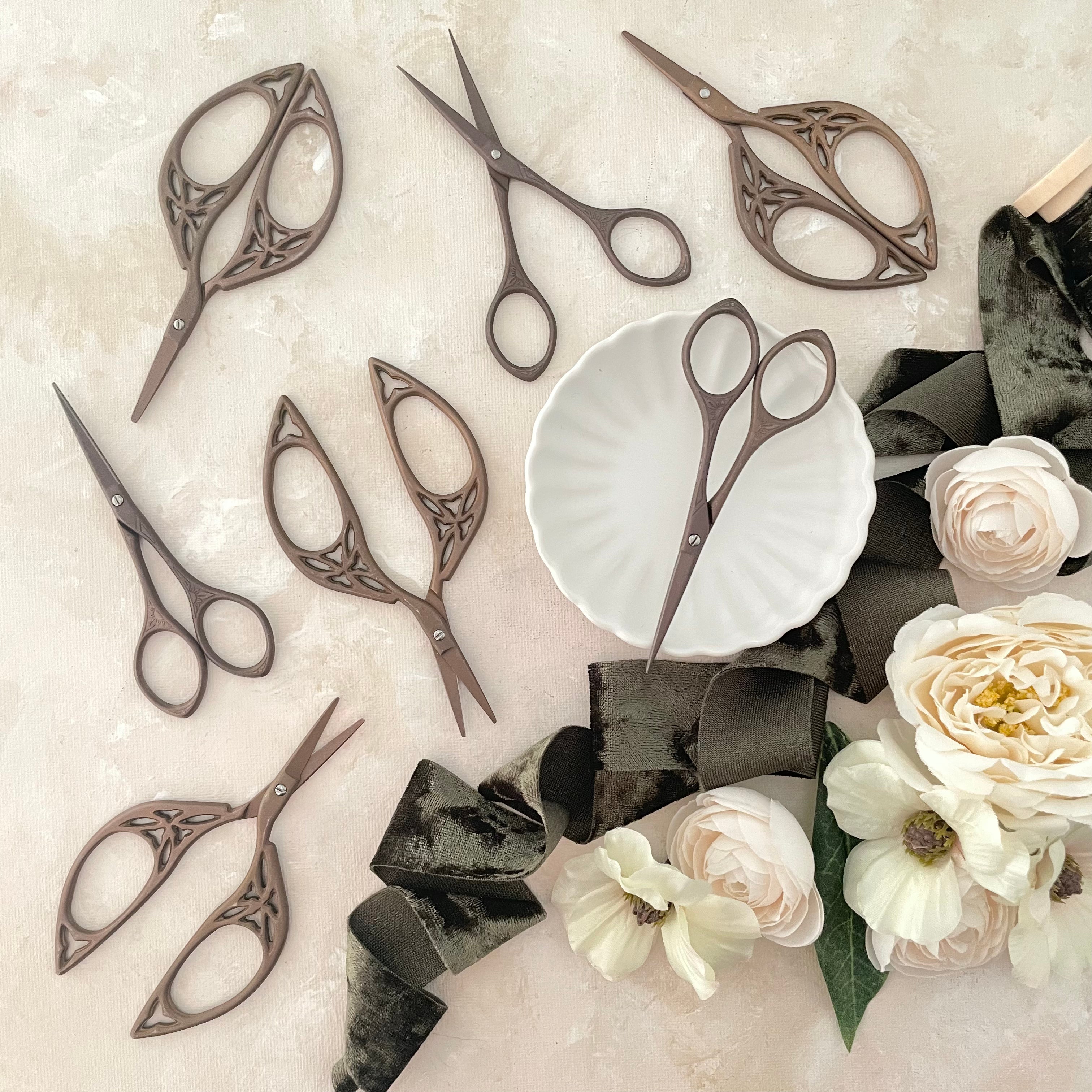 7 Vintage Scissors, one in a Matte white scalloped dish styled with olive green ribbon and ivory florals  - wedding flat lay props from Champagne & GRIT