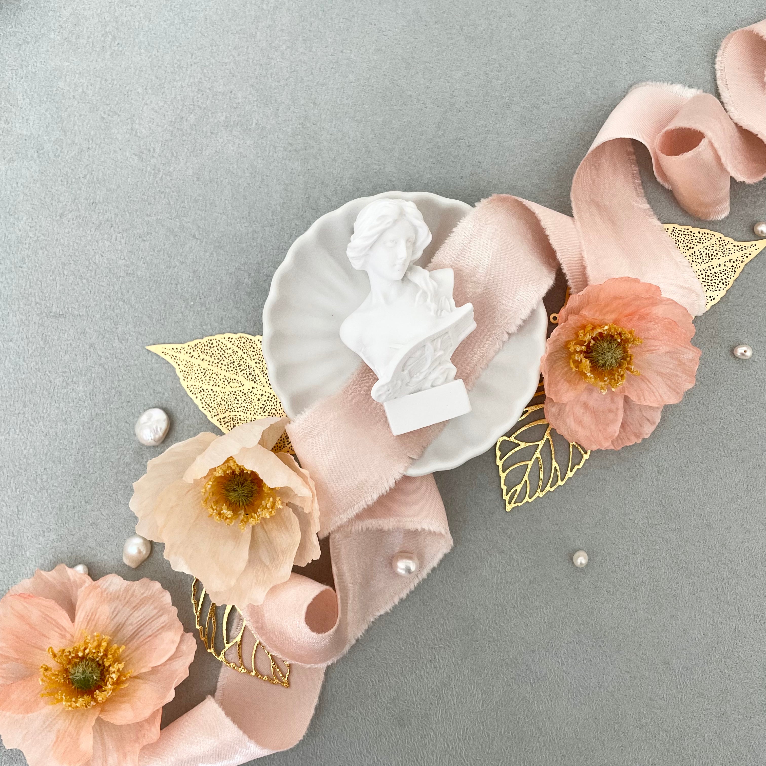 Small vintage figurine on Matte white scalloped dish styled with blush ribbon, 4 styling leaves, and 3 florals - wedding flat lay props from Champagne & GRIT