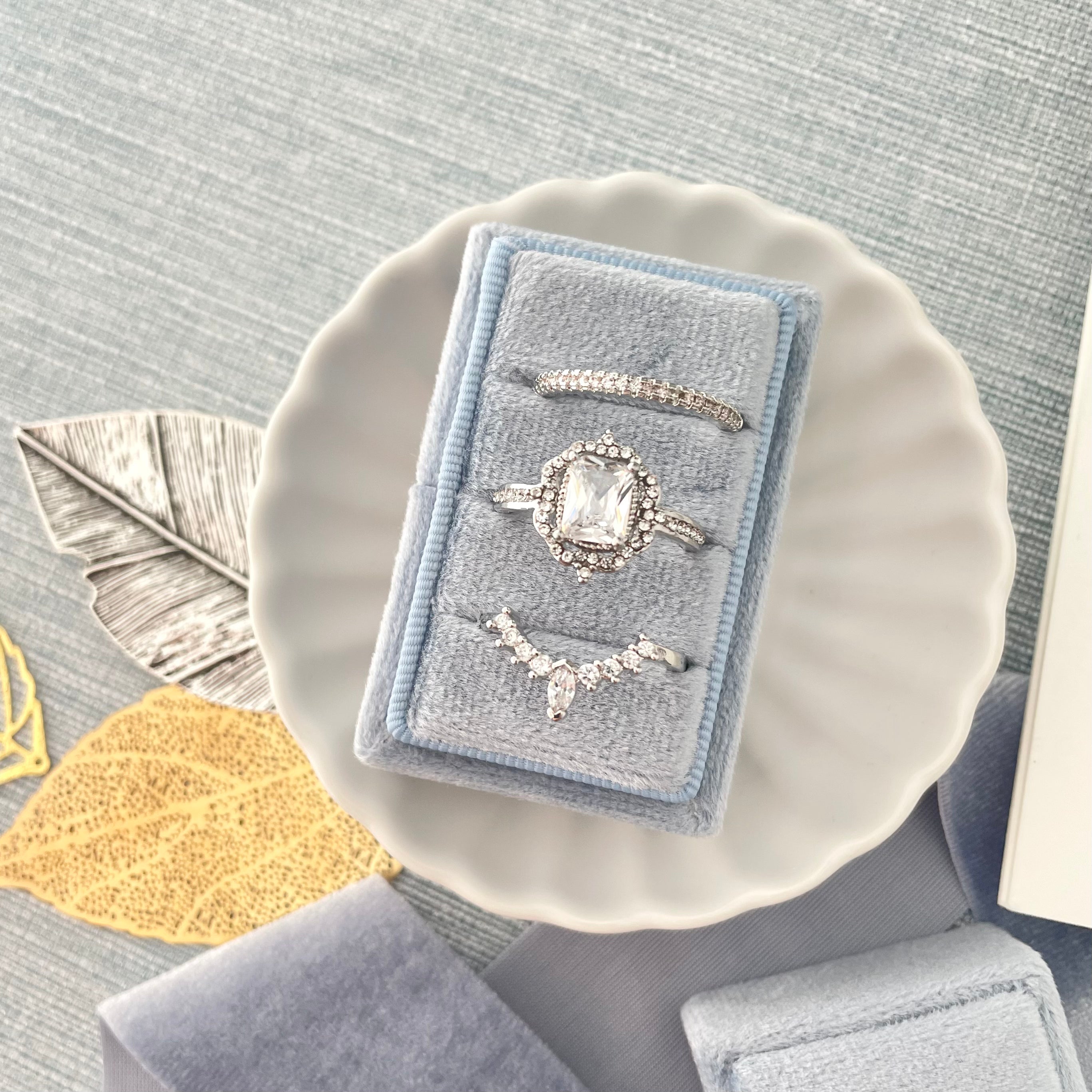 Close up of dusty blue 3 slot ring box in white scalloped dish - wedding flat lay props from Champagne & GRIT