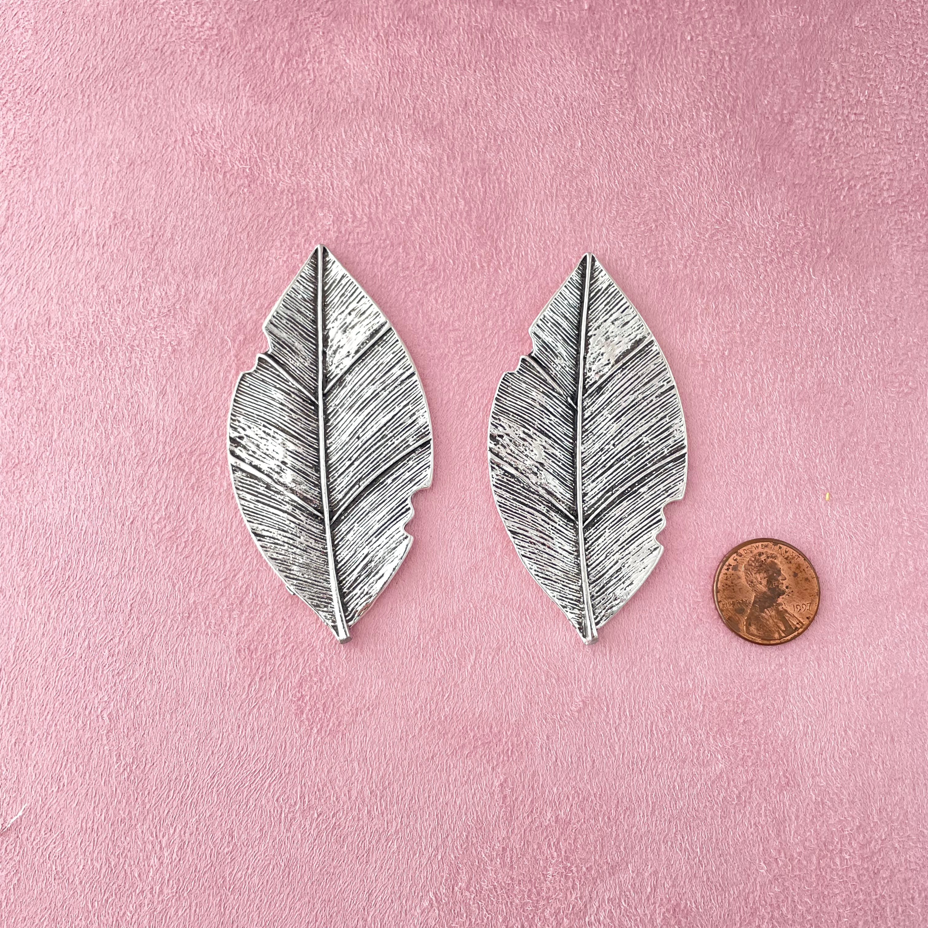 2 large silver with dark accent leaves with penny beside for size reference - wedding flat lay props from Champagne & GRIT