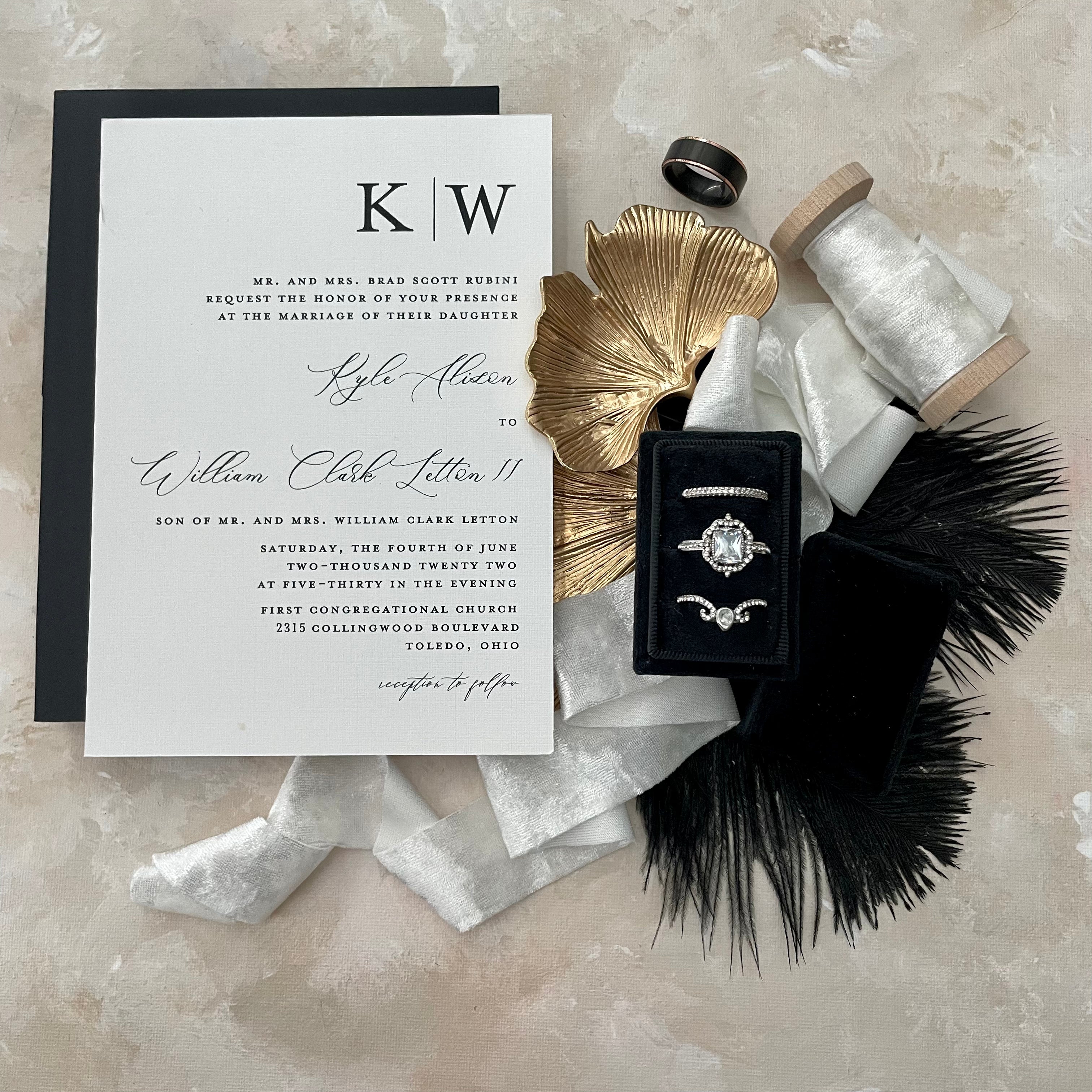 Black triple ring box styled with silver ribbon, Ginkgo Leaf Gold Styling Tray, black and white wedding invitation and black feathers - Flat Lay Props from Champagne & GRIT